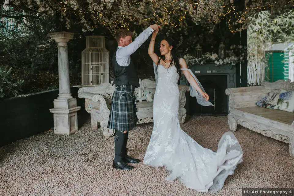 Andrew twirling Hannah beneath flowers and fairy lights at Branxholm Park