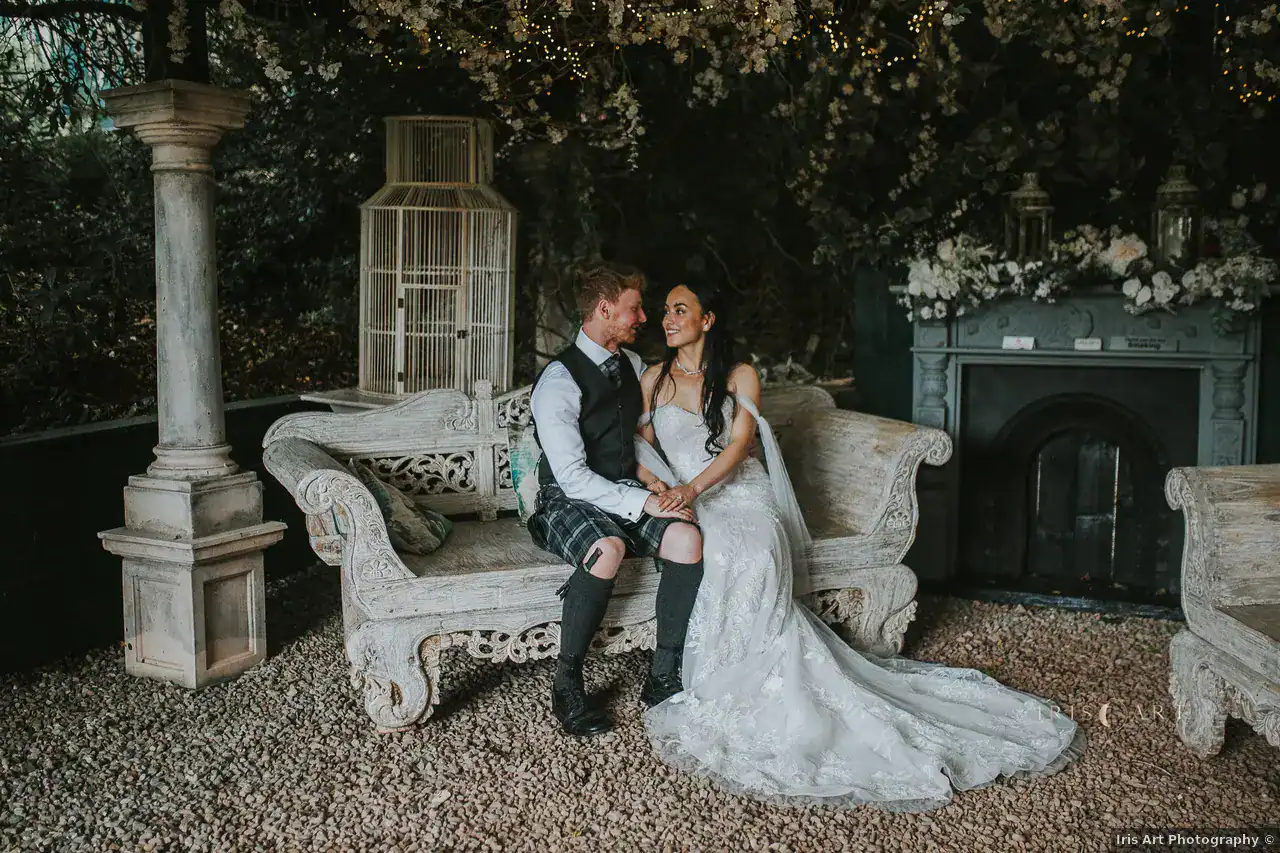 Hannah and Andrew seated together beneath greenery at Branxholm Park