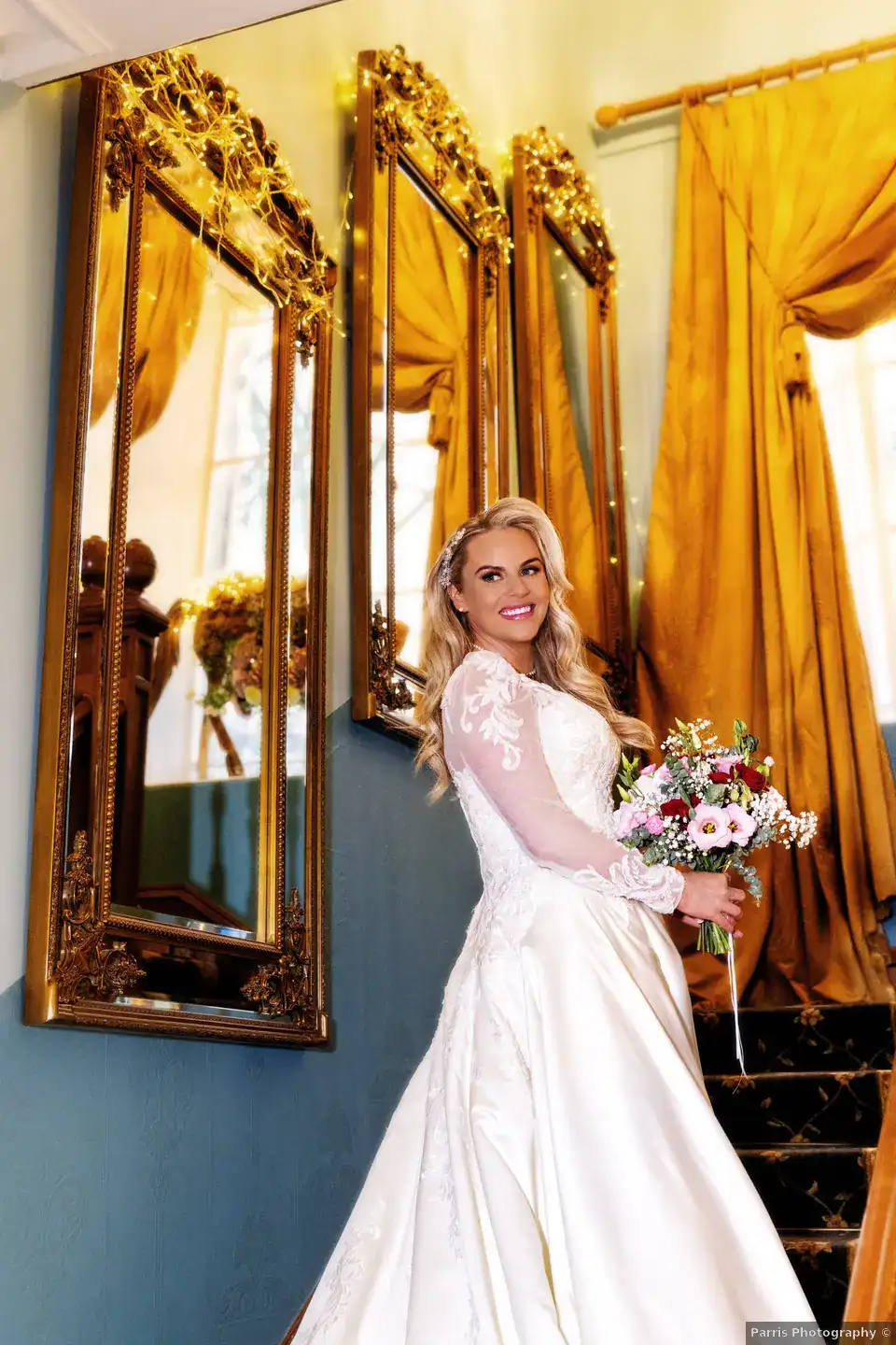 Yvonne holding her bouquet beside gold-framed mirrors at Branxholm Park