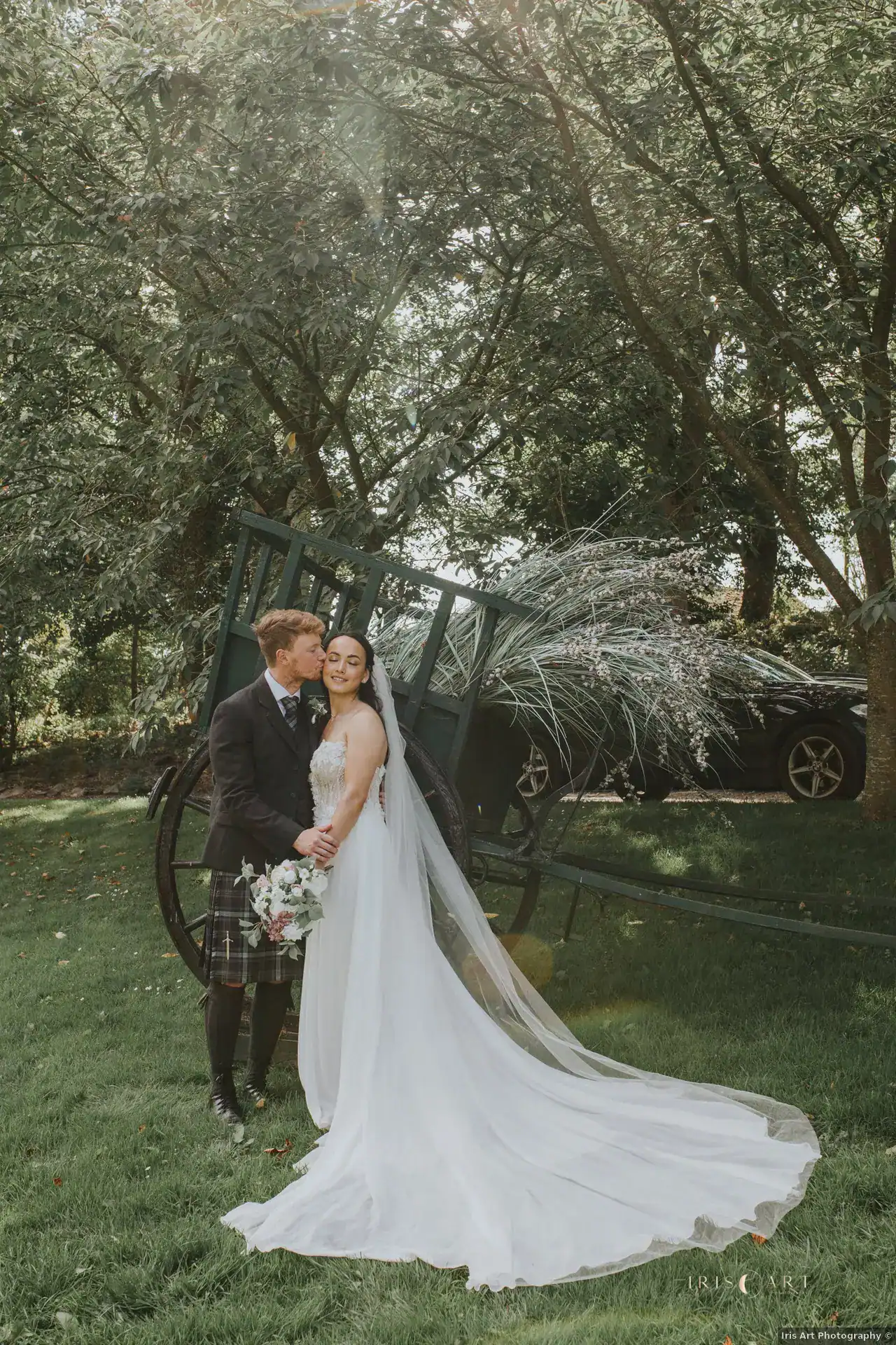 Andrew kissing Hannah on the cheek beside the garden cart at Branxholm Park